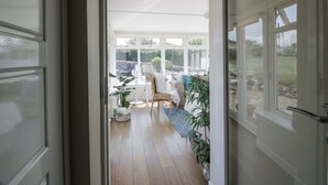 An open doorway leading to a sunlit room with a dining area, a sofa, and potted plants. - Ailsa Shores (Girvan)