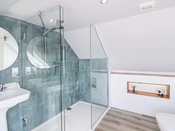 Un baño moderno con cabina de ducha de vidrio, un lavamanos blanco y un estante de madera con una planta.