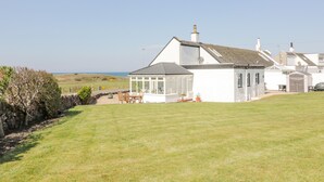A white house with a large glass conservatory, a stone wall, and a grassy lawn. - Ailsa Shores (Girvan)