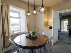 A dining area with a round table, clear chairs, pendant lighting, and a view of the outdoors through a window. - Ailsa Shores (Girvan)