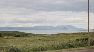 A coastal landscape with a road, grassy fields, and distant mountains.