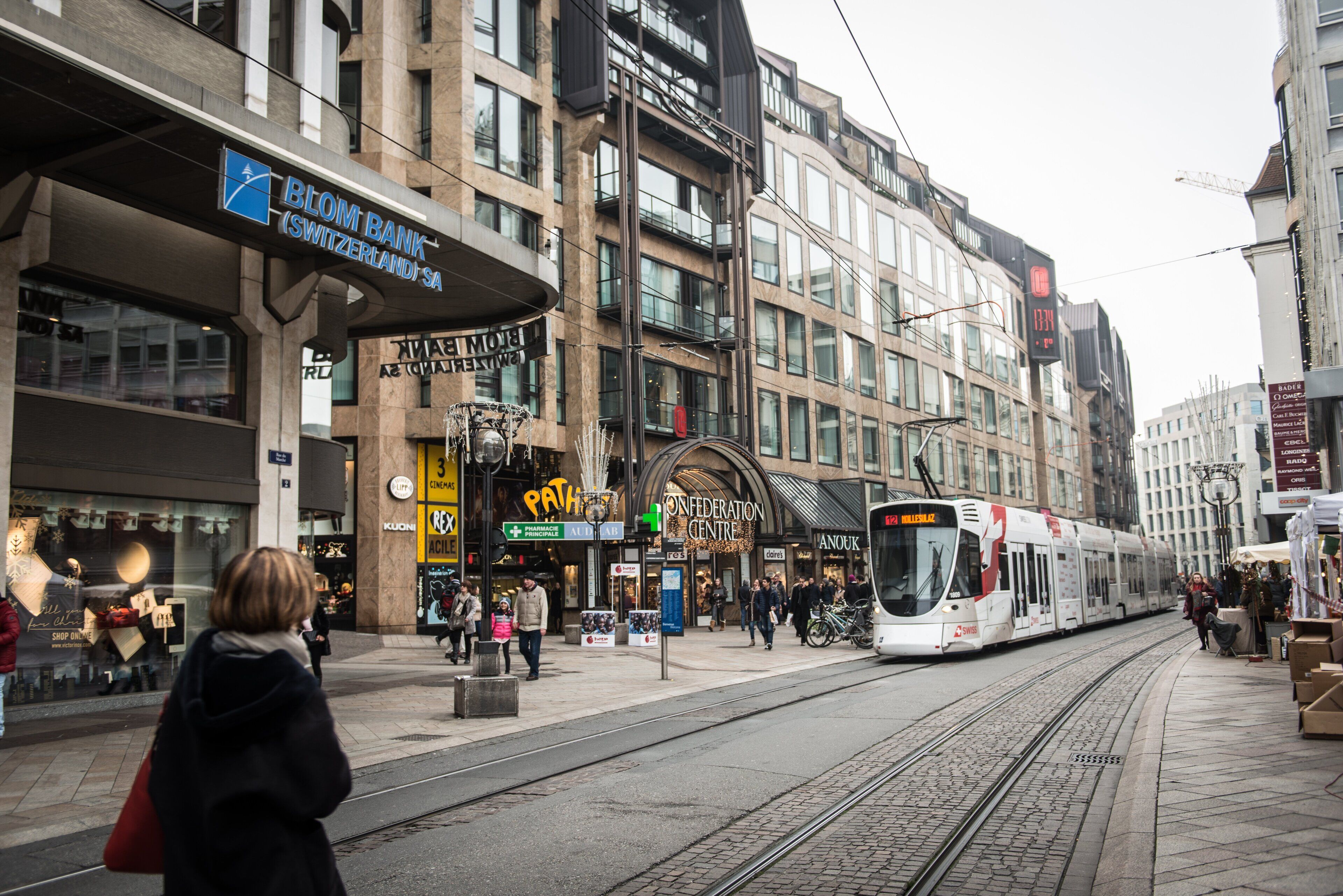 A tram passing by a commercial area with shops and a bank.