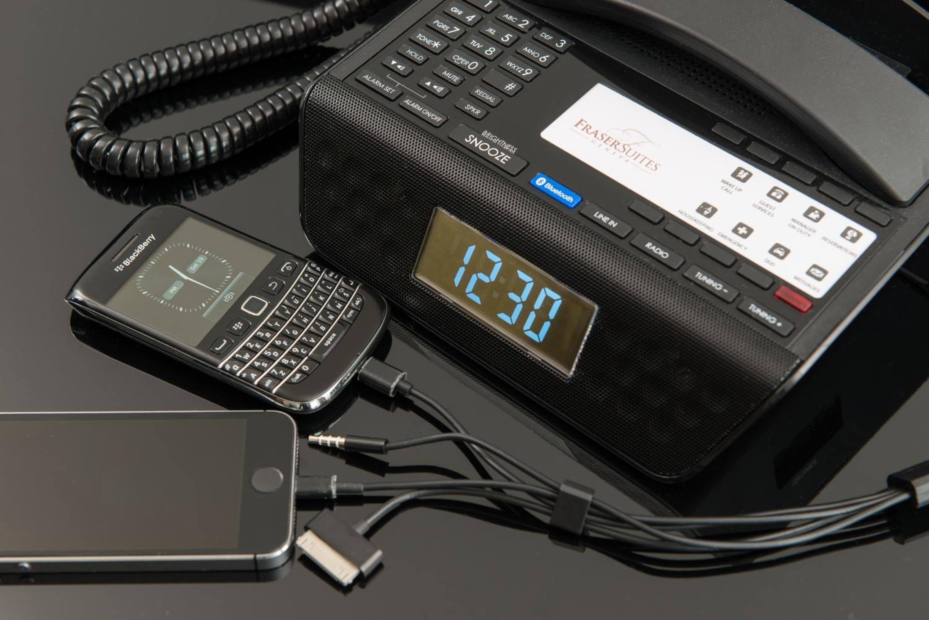 Un téléphone d’hôtel doté d’un écran numérique affichant 12h30, connecté à un appareil Blackberry et à un smartphone.
