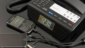 Un téléphone d’hôtel doté d’un écran numérique affichant 12h30, connecté à un appareil Blackberry et à un smartphone.
