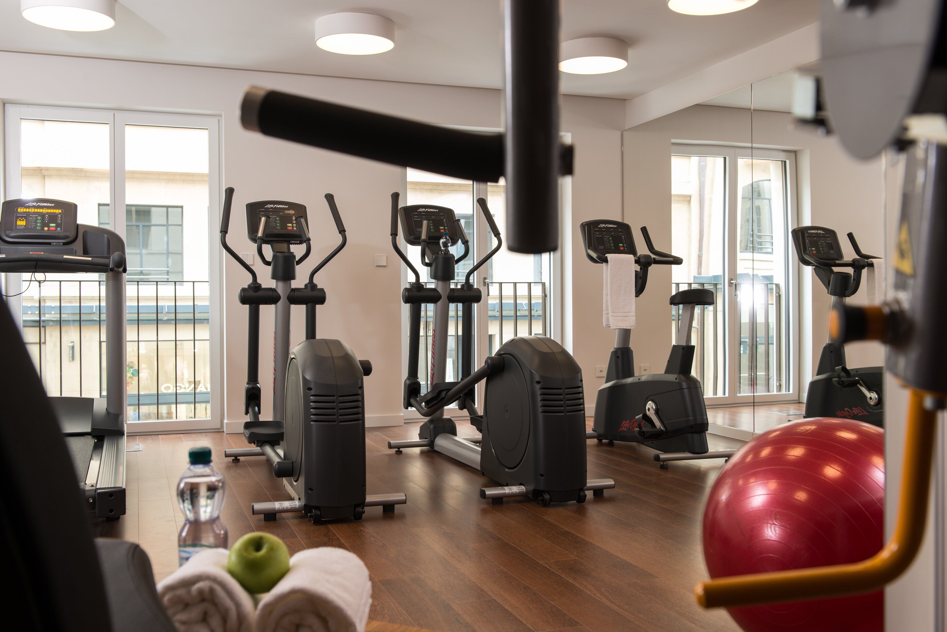 Un gimnasio con diversas máquinas de ejercicio, una pelota roja para hacer ejercicio y una botella de agua en el suelo.
