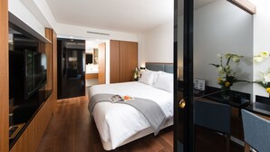 Una habitación de hotel moderna con una cama grande, un escritorio con computadora, un televisor y una puerta de vidrio que da al baño.