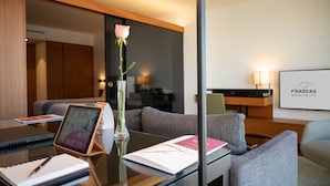 Una habitación de hotel moderna con una mesa de vidrio, una laptop, una tableta, un cuaderno y un jarrón con una rosa.
