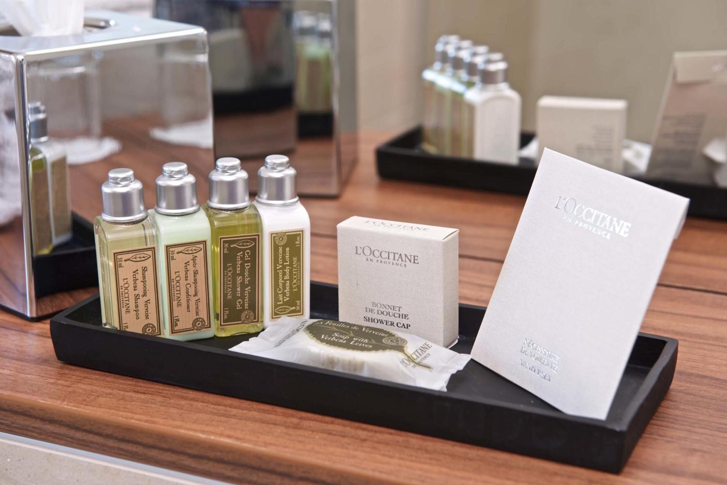 A display of L'OCCITANE shower cap and toiletries on a wooden tray.