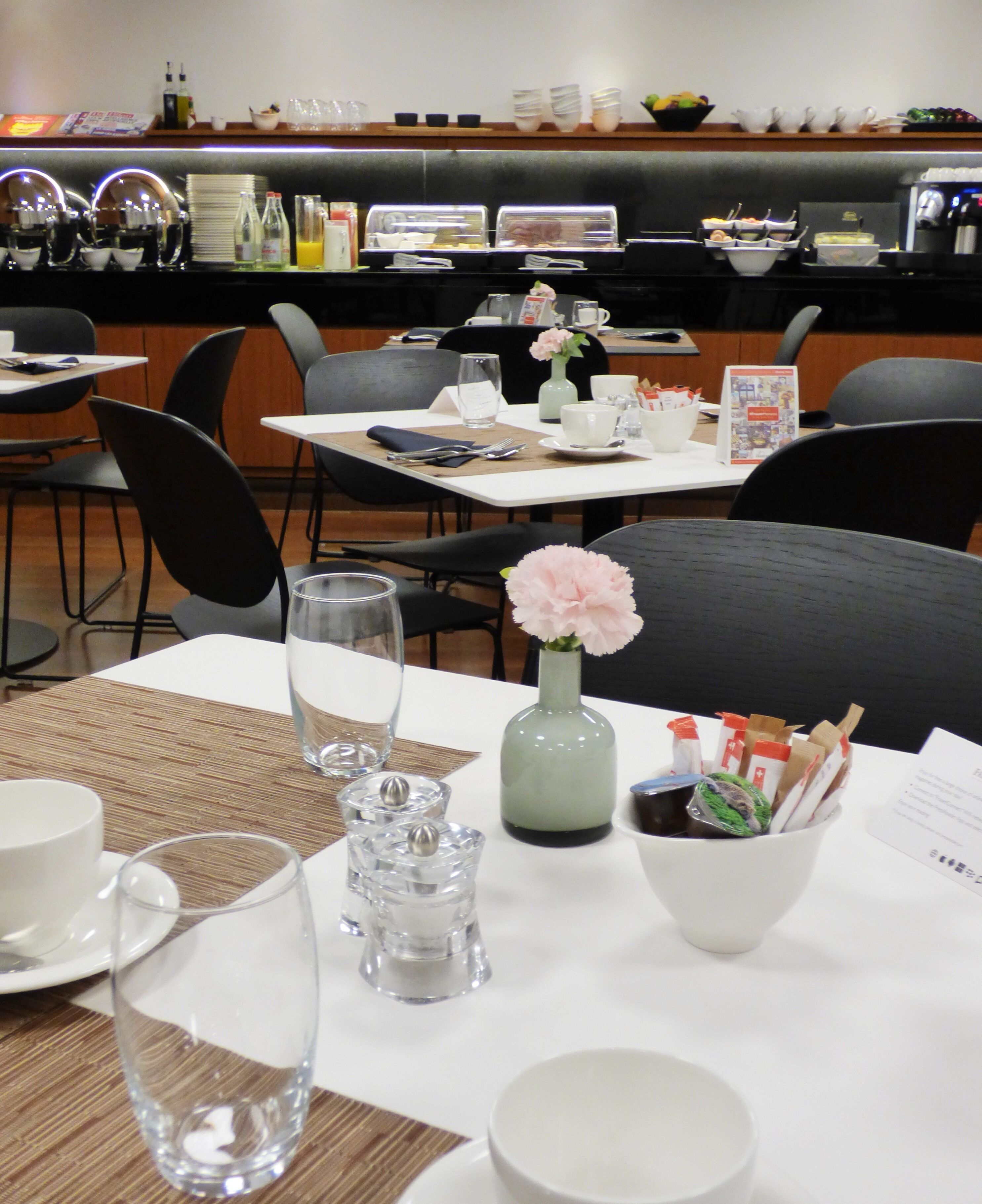 A dining area with tables set for breakfast, including plates, cups, and a vase with flowers.