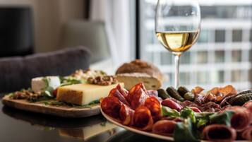 A table with a variety of cheeses, cured meats, and pickles, accompanied by a glass of white wine.