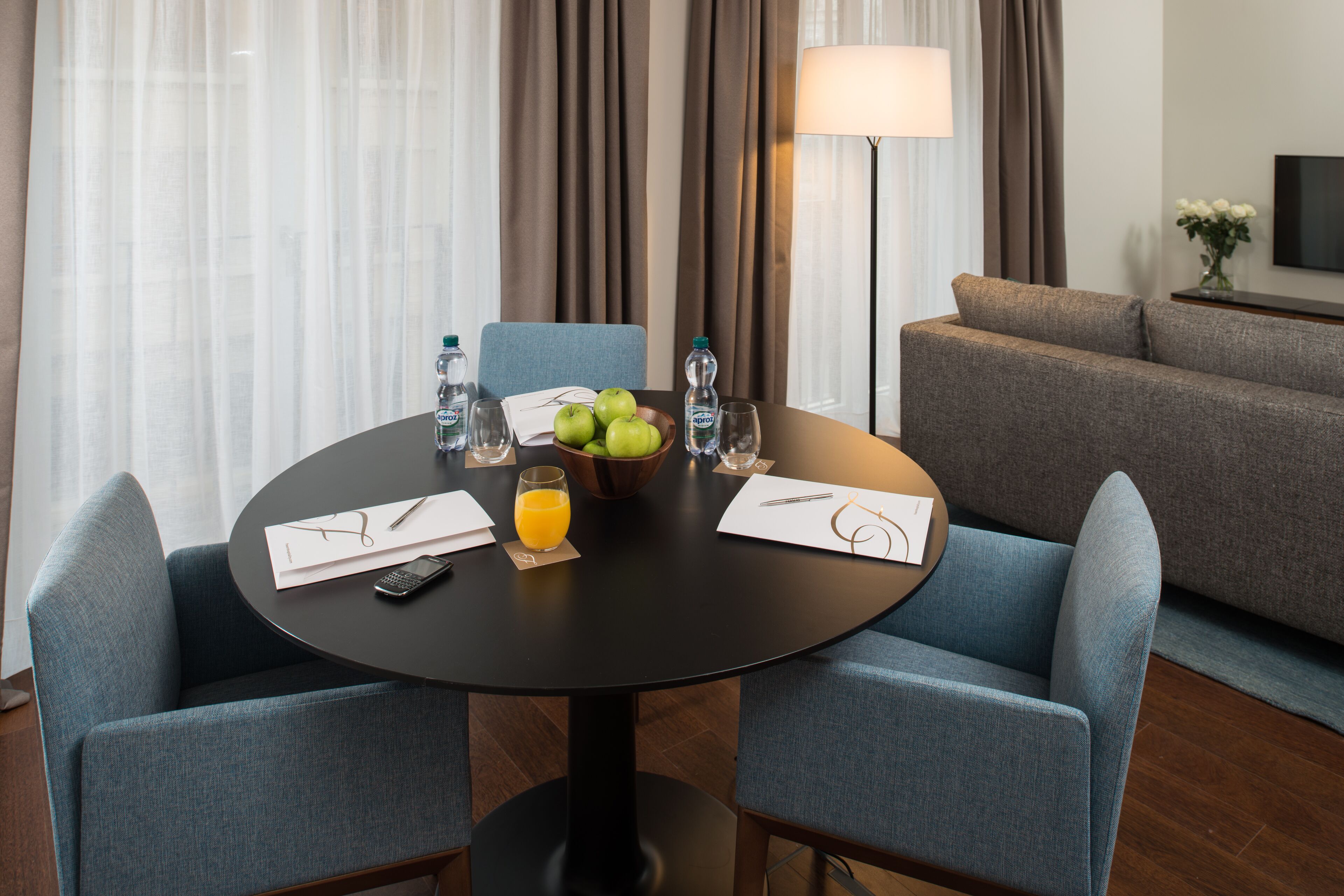 Une chambre d’hôtel avec une table ronde dressée pour deux personnes, un canapé, une lampe et un téléviseur fixé au mur.