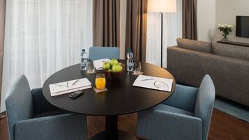 Une chambre d’hôtel avec une table ronde dressée pour deux personnes, un canapé, une lampe et un téléviseur fixé au mur.