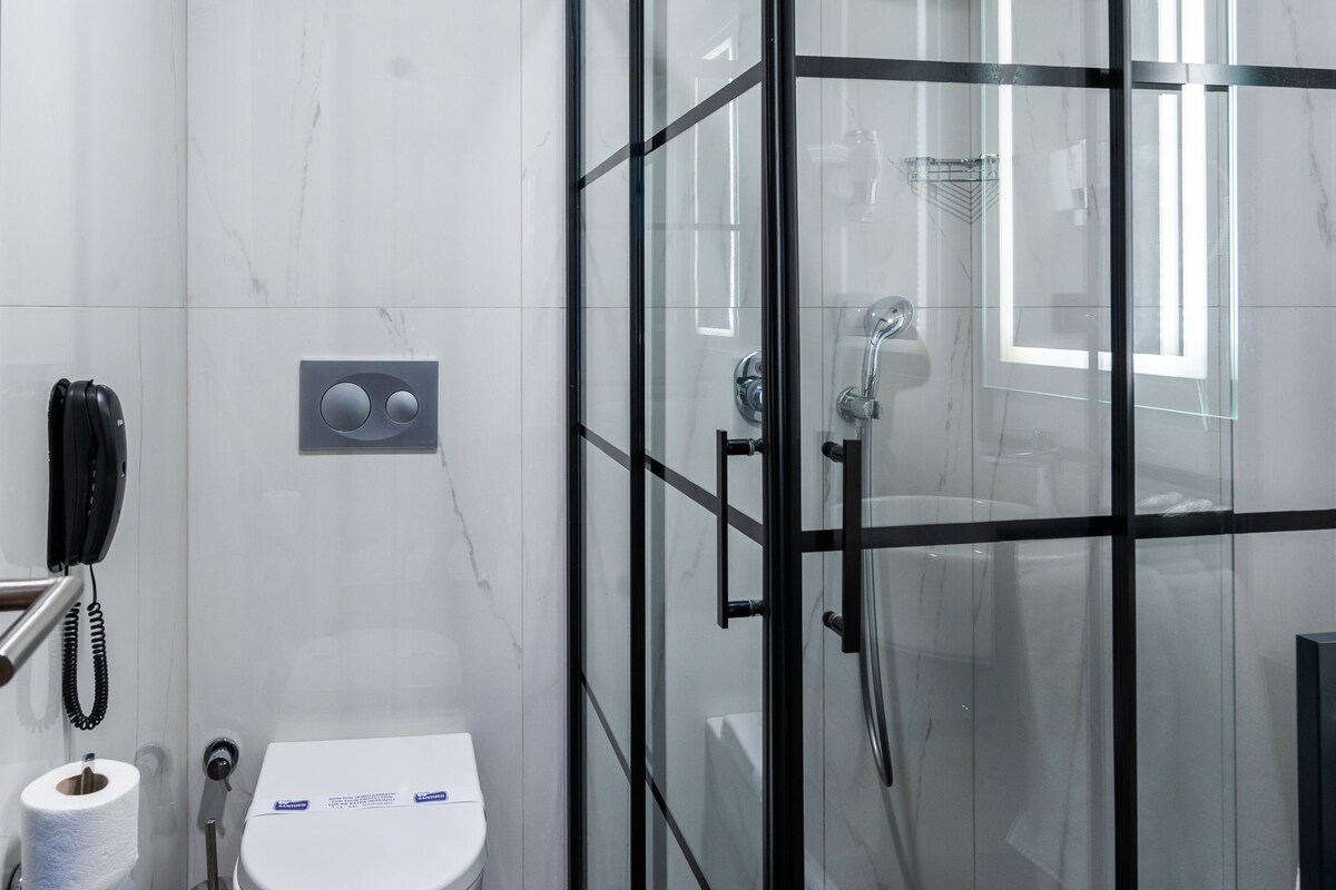 A modern bathroom with a toilet, a shower enclosure, and a marble wall.
