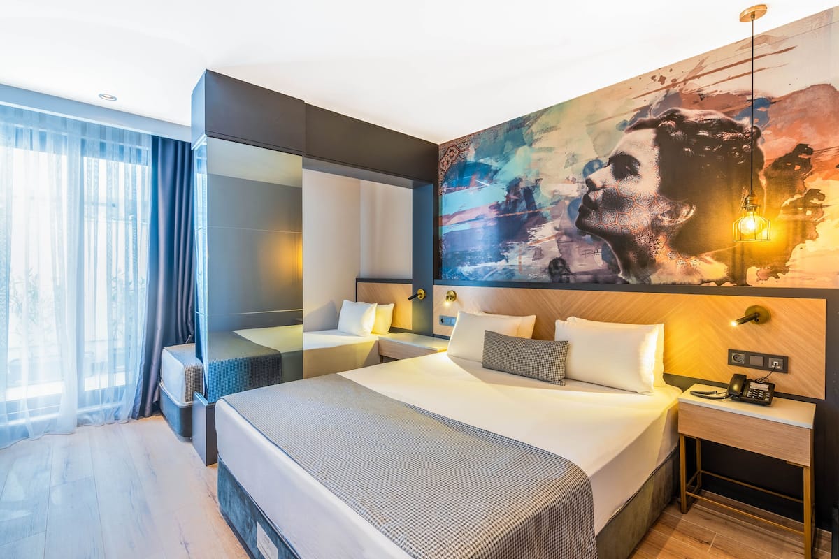 A modern hotel room with a large bed, bedside tables, a mirror, and a large abstract painting on the wall.
