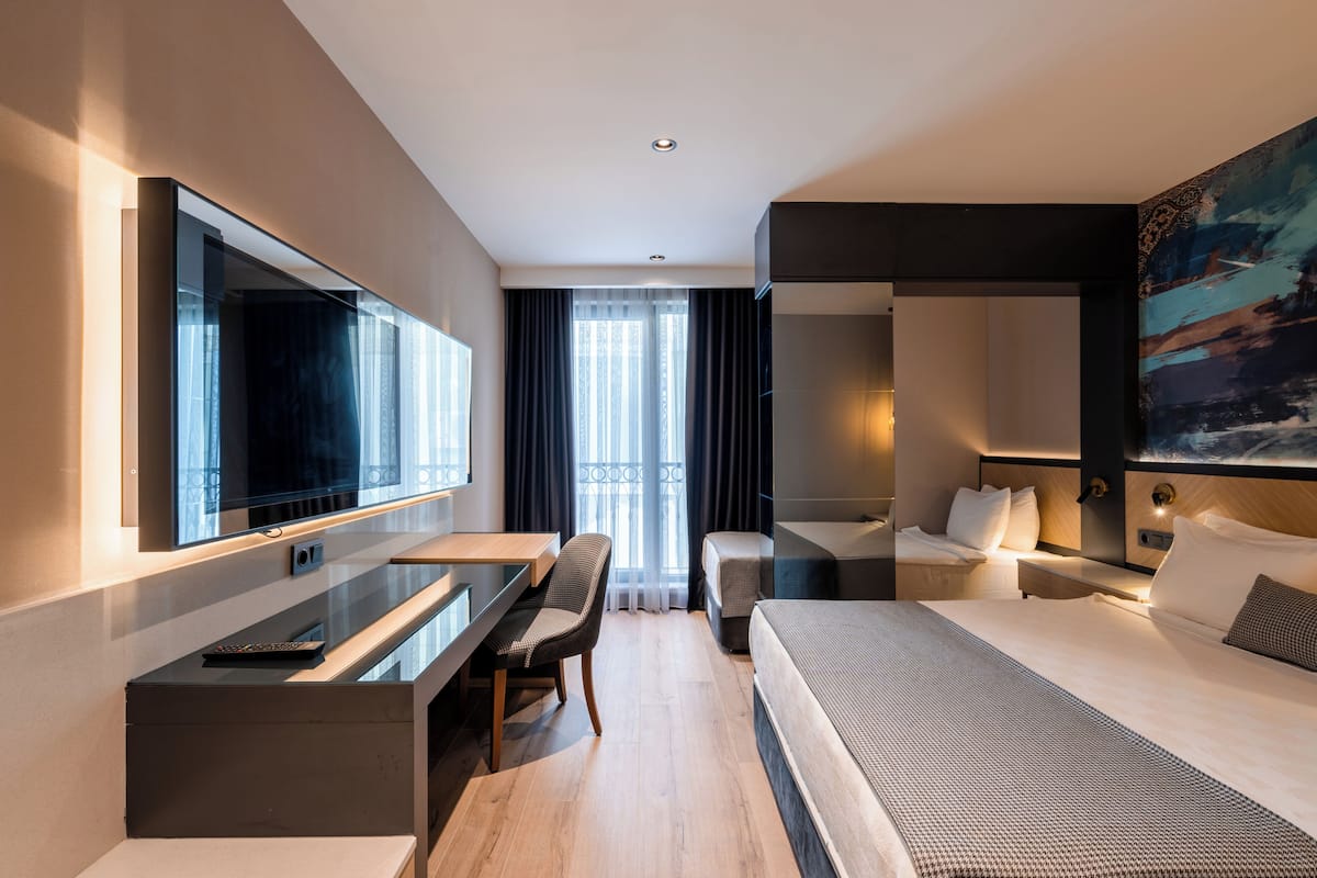 A modern hotel room with a large bed, a desk, a chair, and a television.