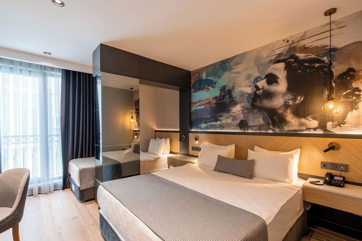 A hotel room with a large bed, a smaller bed, a desk, a chair, and a large painting on the wall.