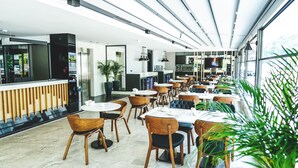 A modern restaurant with round tables and wooden chairs, a bar area, and large windows allowing natural light. - Ni Hotel Lara (Antalya)