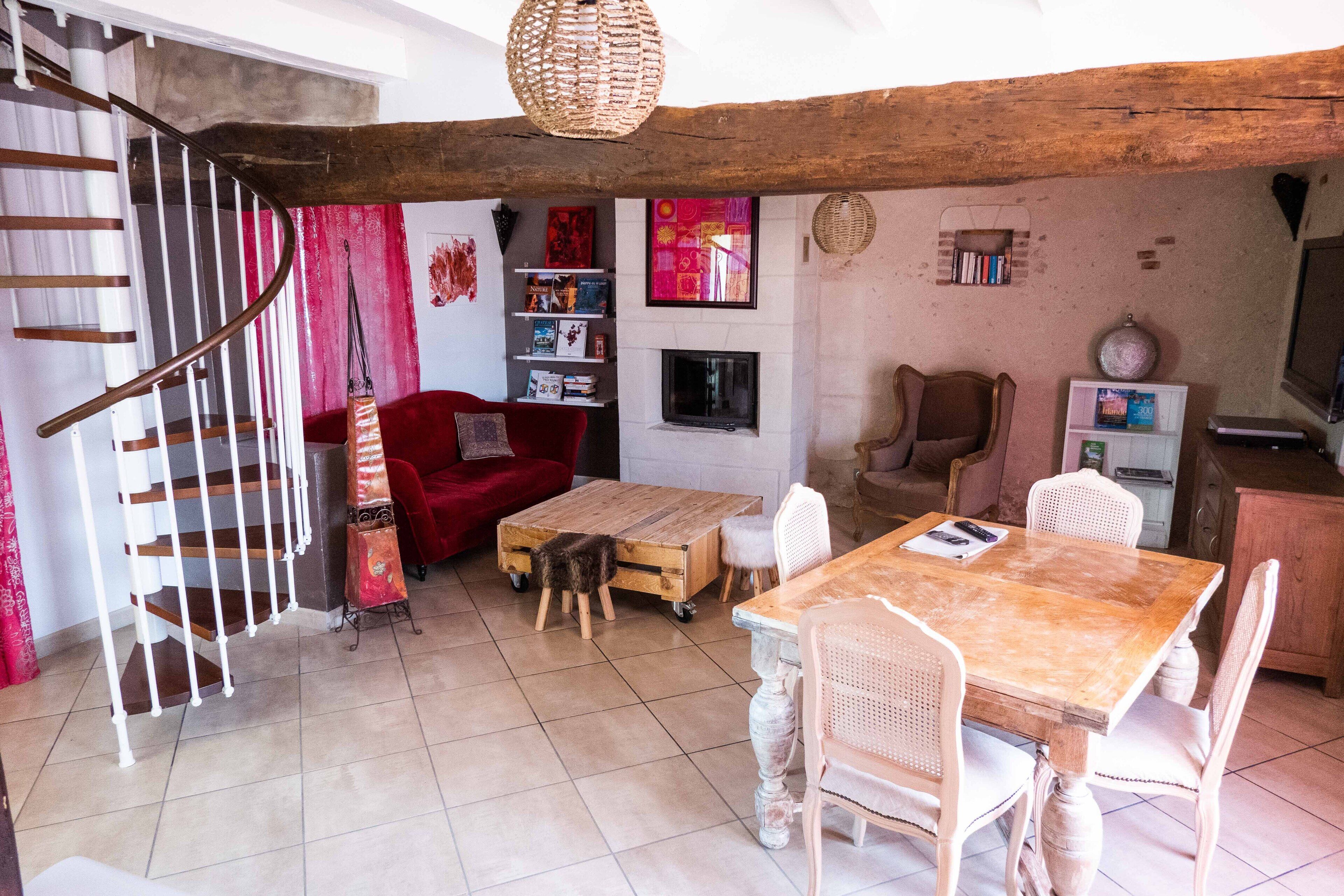 A cozy living room with a wooden staircase, a red sofa, a wooden coffee table, and a dining table with chairs.