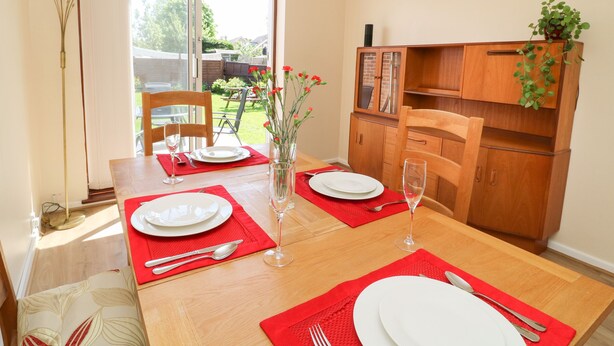 A dining area with a wooden table set for two, a vase with flowers, and a cabinet with a plant. - 4 Ranby Drive (Hornsea)