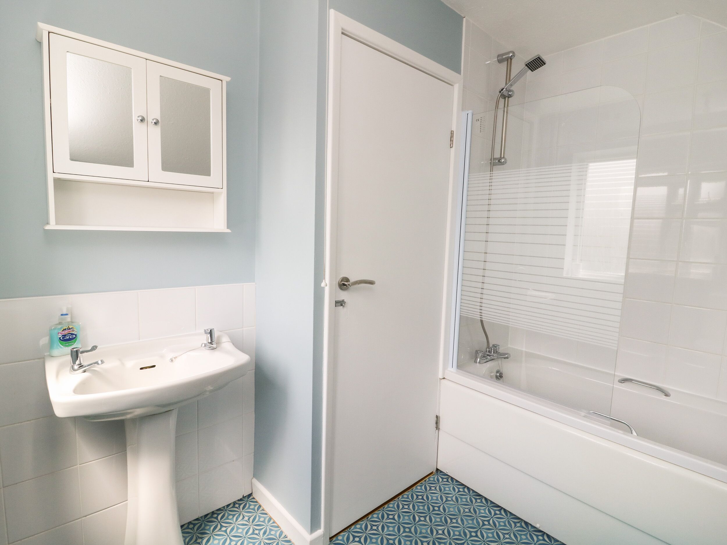 A bathroom with a white sink, a cabinet, and a shower enclosure.
