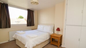 A bedroom with a bed, a nightstand, a lamp, a wardrobe, and a window with curtains. - 4 Ranby Drive (Hornsea)