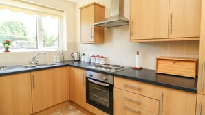 A modern kitchen with wooden cabinets, a stainless steel range hood, a built-in oven, and a window providing natural light. - 4 Ranby Drive (Hornsea)