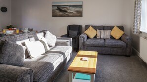 A living room with two grey sofas, a wooden side table, and a painting of a boat on the wall. - Dabbling Ducks (Whitby)