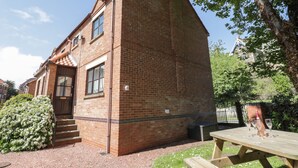 A brick building with a door and windows, a picnic table, and a tree in the background. - Dabbling Ducks (Whitby)