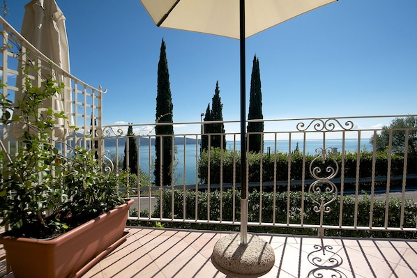 A balcony with a view of the sea, a potted plant, and a metal fence.
