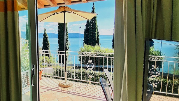Un balcón con vista a un lago, una pérgola y una barandilla de metal.