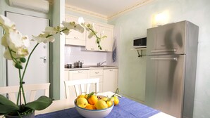 Una cocina con armarios blancos, un refrigerador de acero inoxidable, un microondas y un tazón de fruta sobre la mesa.