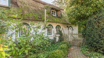 Een traditioneel huis met rieten dak, muur bedekt met klimop en een houten poort.