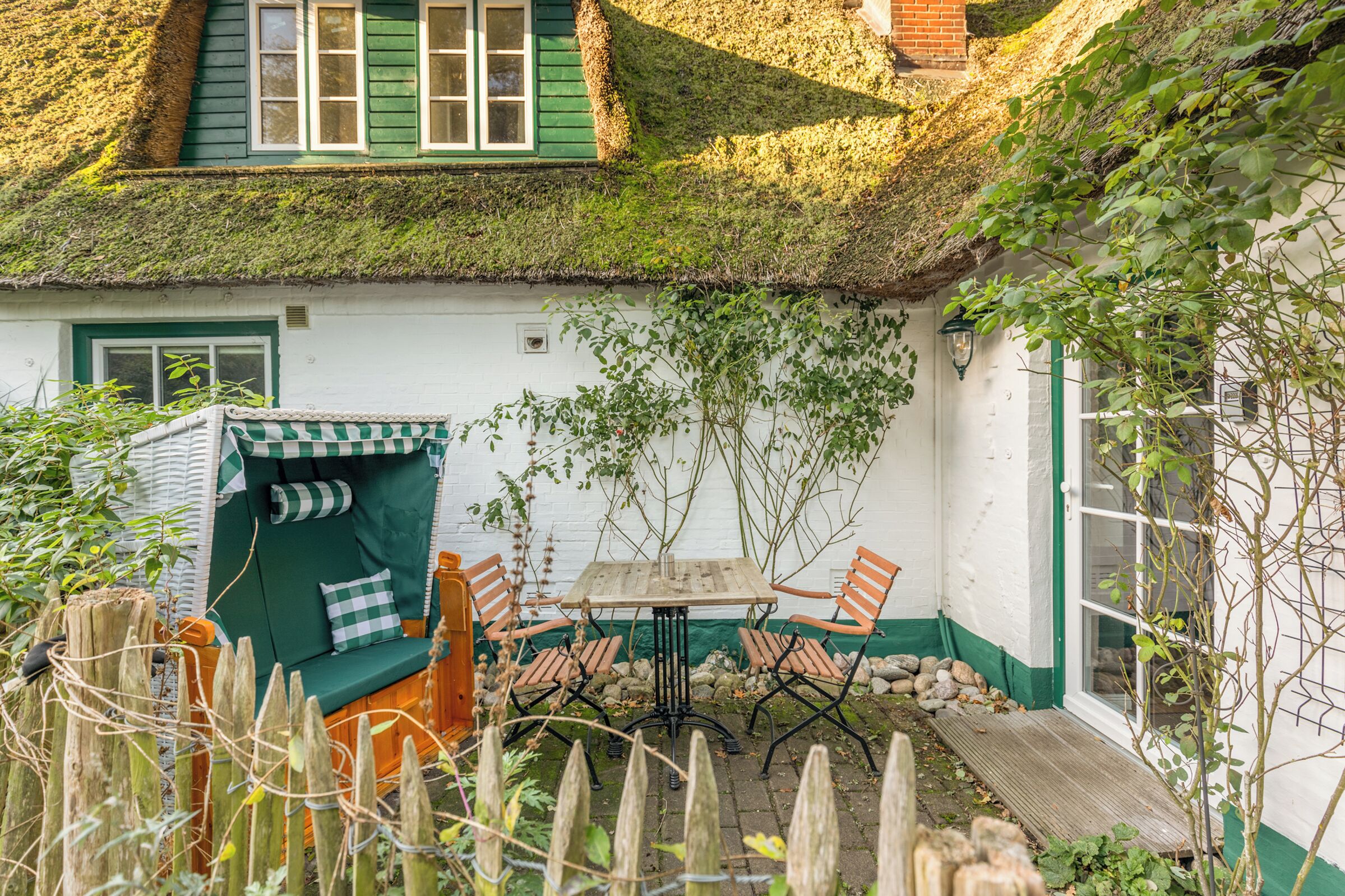 Une maison traditionnelle avec un toit de chaume, une table en bois avec des chaises et un petit jardin.