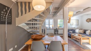 A modern interior with a wooden dining table, grey chairs, a spiral staircase, and a living area with a sofa and a coffee table.