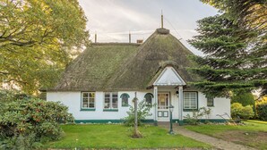 A traditional house with a thatched roof, white walls, and green trim.