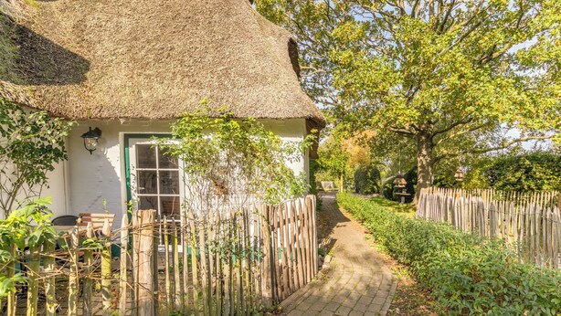 A thatched-roof cottage with a paved pathway leading to a wooden fence.