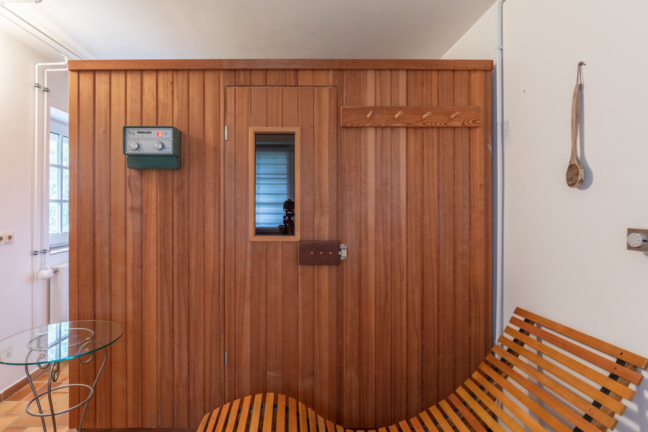 A wooden-paneled room with a bench, a glass table, and a wooden bench.