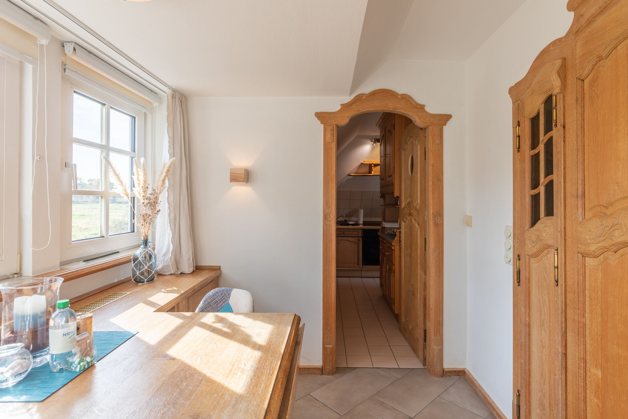 A hallway with a wooden door, a window with curtains, and a table with various items.