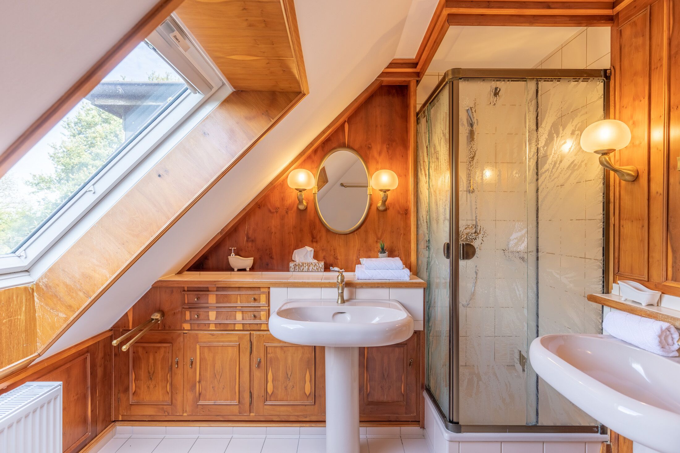 Ein Badezimmer mit Holzschränken, einem weißen Waschbecken und einer Duschkabine aus Glas.