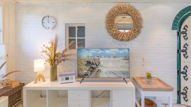 Pared de ladrillo blanco con un reloj, una fotografía enmarcada de la playa, un espejo de madera y una puerta con detalles de hierro negro.