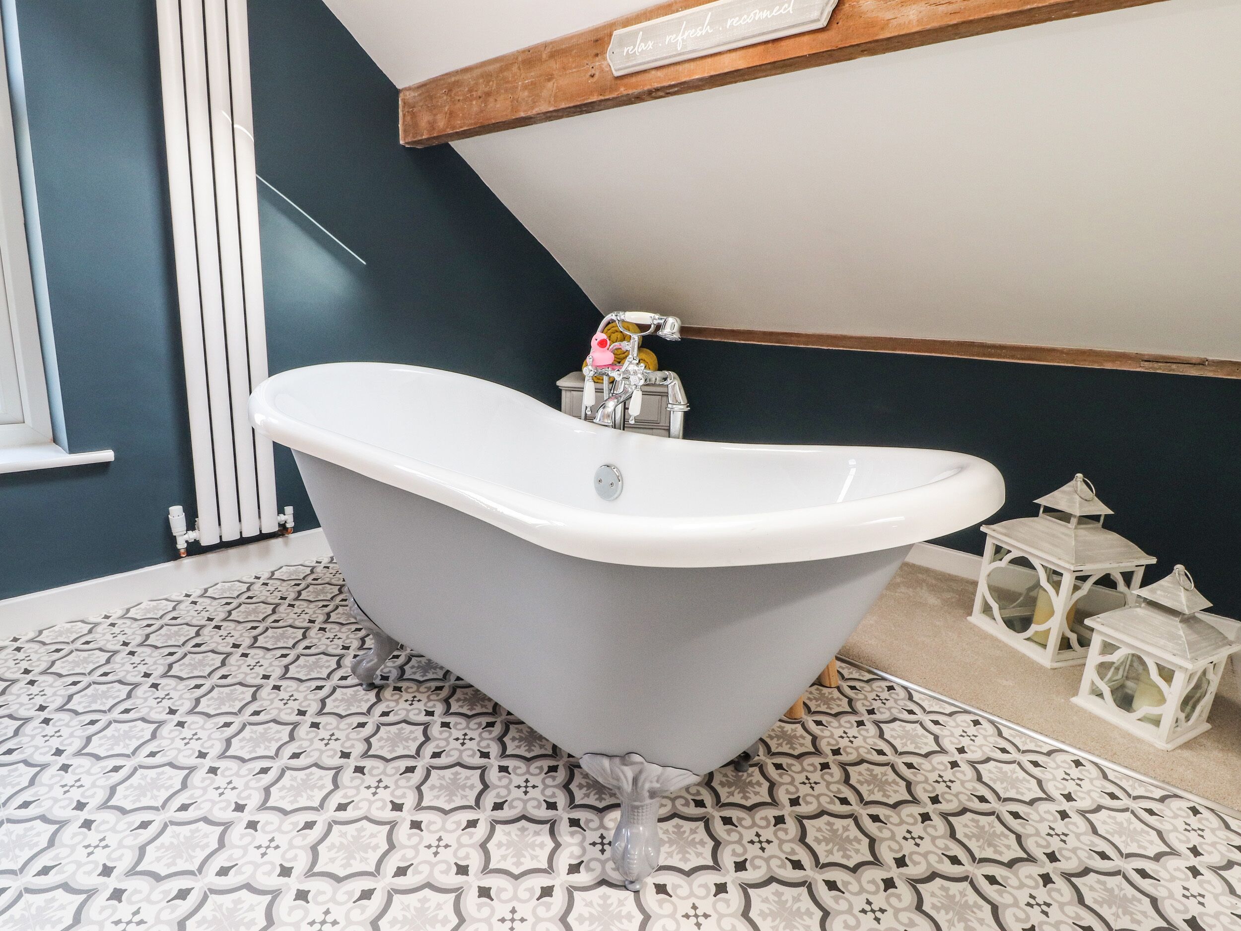 A modern bathroom with a freestanding bathtub, a radiator, patterned floor tiles, and decorative lanterns.