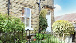A brick house with a white door, a window, and a black metal fence in the foreground. - No 19, Haworth (Keighley)