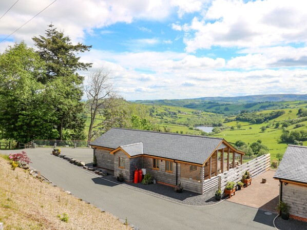 A small lodge with a stone facade, a sloped roof, and a view of rolling hills and a lake. - The Larches (Llanidloes)