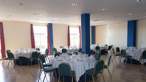 A spacious banquet hall with round tables set for dining, teal chairs, and large windows with red curtains. - Hotel ELE Puerta de Monfrague (Malpartida de Plasencia)