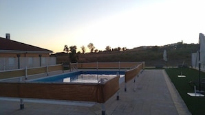 A rectangular pool with a wooden deck, surrounded by a white fence and a paved walkway. - Hotel ELE Puerta de Monfrague (Malpartida de Plasencia)
