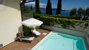 A swimming pool with lounge chairs and an umbrella, surrounded by greenery and a view of the sea.
