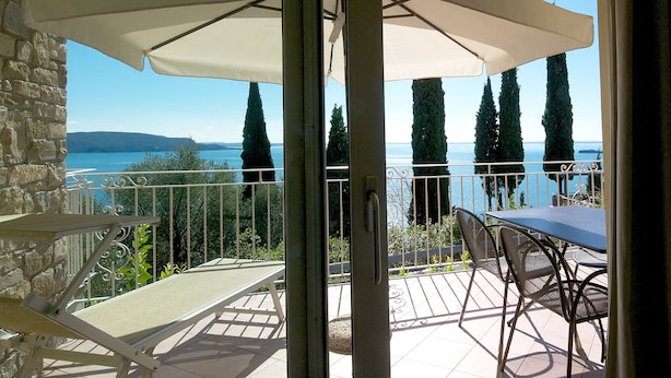A balcony with a table and chairs, overlooking a body of water and trees.