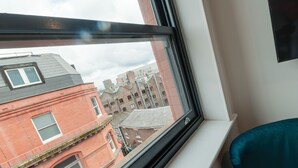 Et vindue med udsigt til en rød murbygning og en hvid bygning med solsejl.