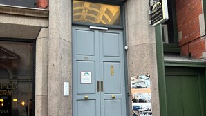 En grå dør med dobbeltfløje, et messinggreb, et skilt for HappyDays Apartments, og et lille vindue med et skilt der siger 'Gæste Check-in'.