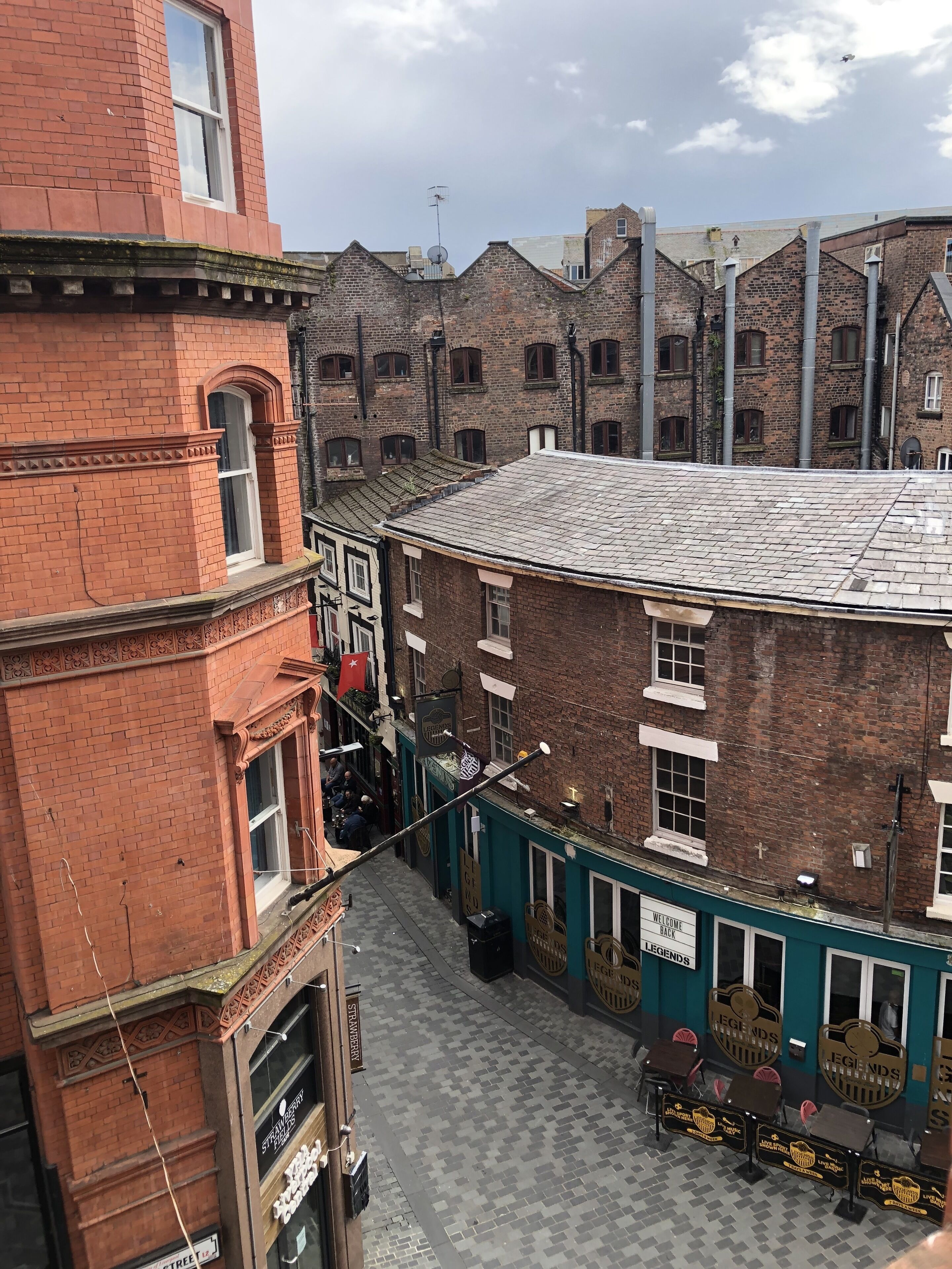 A narrow street with brick buildings, a pub named 'LEGENDS', and a sign for 'STRAWBERRY STREET'.